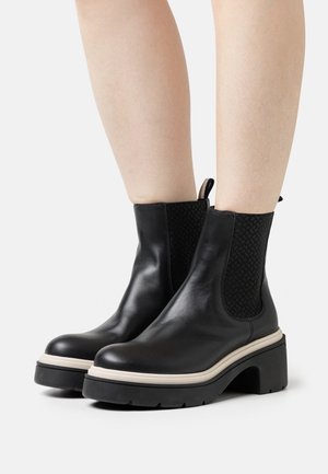 Black leather ankle boots with textured elastic side panels and white accent soles. Chunky black platform heels provide stability and height.