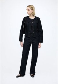 Casaco de ganga escura e jeans de cintura alta com silhueta ajustada. O casaco possui fechos de botão e dois bolsos frontais. Sapatilhas pretas e mala.