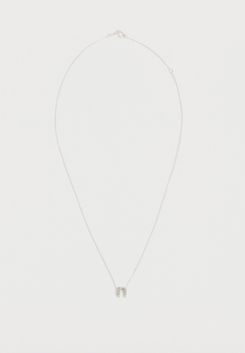 Collier délicat en chaîne argent avec un petit pendentif en forme de fer à cheval centré sur fond blanc.