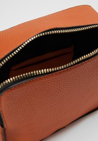 Interno di borsa in pelle arancione con trama, con fodera nera, dotato di una cerniera dorata e una piccola tasca per l'organizzazione.