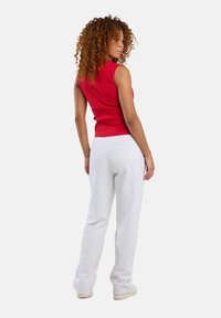 Red sleeveless top with a fitted design, paired with gray sweatpants. Model faces slightly away, showcasing curly hair and relaxed fit.