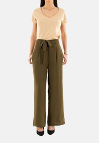 T-shirt beige a scollo a V abbinato a pantaloni verde oliva a vita alta con cintura annodata. I pantaloni sono a gamba larga con un tessuto strutturato.