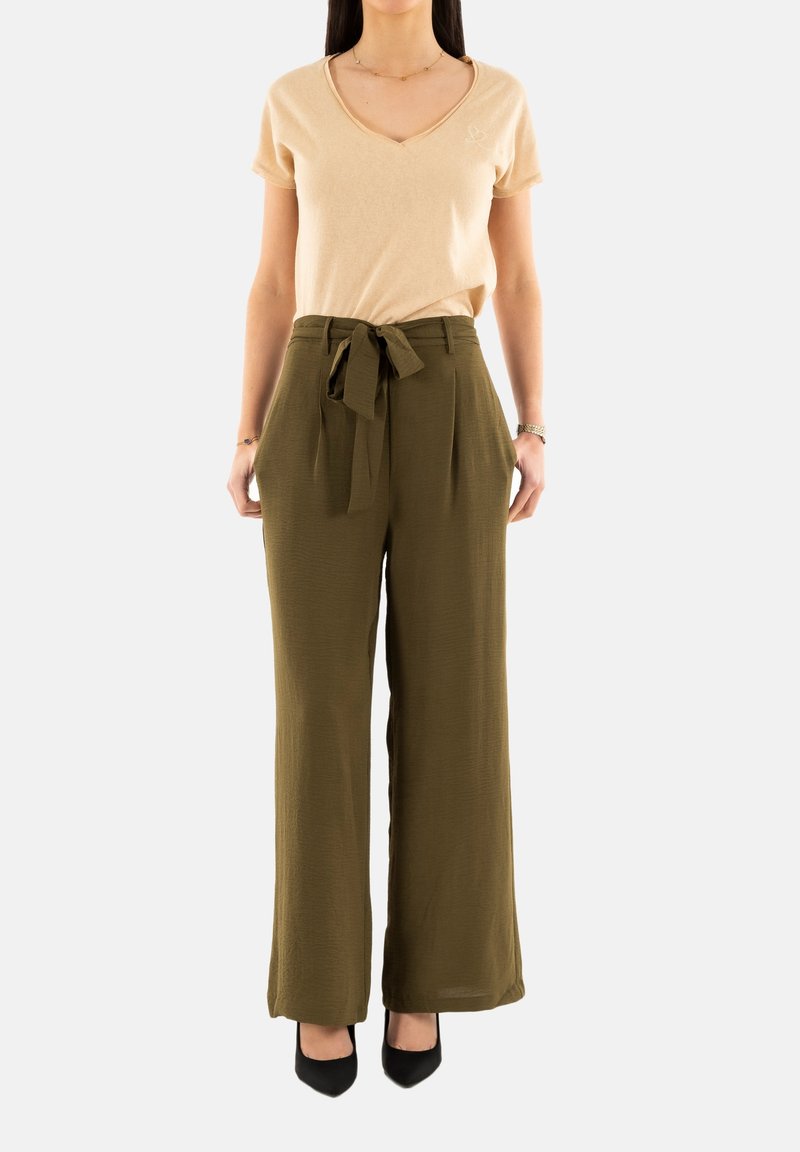 T-shirt beige a scollo a V abbinato a pantaloni verde oliva a vita alta con cintura annodata. I pantaloni sono a gamba larga con un tessuto strutturato.