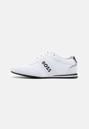 Biały niski sneaker z czarną podeszwą, logo „BOSS” po boku, sznurowane zapięcie i szary detal na pięcie, pokazany z profilu na jednolitym tle.