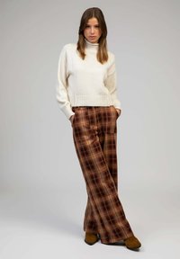 Un pull en col roulé de couleur crème associé à un pantalon large à carreaux marron. Le pantalon présente un motif à carreaux avec des teintes de brun foncé et de beige.