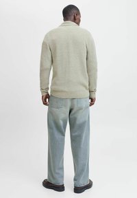 Pull en tricot vert clair avec un motif texturé, col châle et poignets côtelés, associé à un pantalon en denim bleu clair ample.