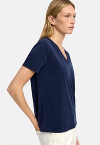 Granatowa koszulka z dekoltem w serek, wykonana z miękkiej, lekkiej tkaniny, z krótkimi rękawami i luźnym krojem, charakteryzująca się gładką fakturą i prostym fasonem.