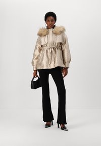 Bežna puffer jakna s vzorcem, sijočim materialom, kapuco iz krzna in pasom. V kombinaciji z črnimi rebrastimi hlačami in majhno črno torbico.