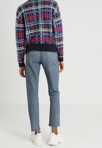 Strickpullover mit einem mehrfarbigen Karomuster, kombiniert mit hellblauen Jeans und weißen Sneakers, mit einem cropped Saum und lockerer Passform.
