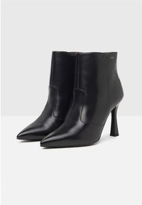 Bottines en cuir noir avec des bouts pointus, talons fins, design épuré et couture extérieure. Détail de logo subtil sur le côté.