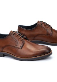 Chaussures en cuir marron à lacets avec une finition lisse, un bout arrondi, des coutures contrastées et une semelle en caoutchouc pour l'adhérence.