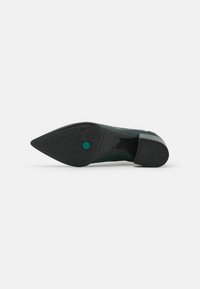 Chaussure verte avec un bout pointu, une tige texturée et une semelle en caoutchouc noir comportant un accent circulaire. Conçue pour un look ajusté.