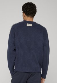 Pull bleu marine avec une finition texturée, ourlet côtelé et motif contrasté sur les épaules. Étiquette cousue à l'arrière du col.