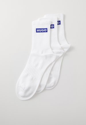 Calze bianche a coste con logo blu "HUGO" sulla parte superiore. Materiale morbido, lunghezza standard alla caviglia e design senza cuciture sulla punta. Set di tre paia.