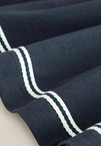 Tela azul oscuro con rayas dobles blancas y verde oscuro a lo largo de los bordes, mostrada en primer plano con costuras visibles y capas dobladas.