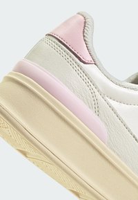 Weißes Leder sneaker mit einem hellrosa Akzent an der Ferse. Strukturiertes Mittelsohle in Creme mit gerilltem Muster für besseren Halt. Insgesamt glatte Oberfläche.