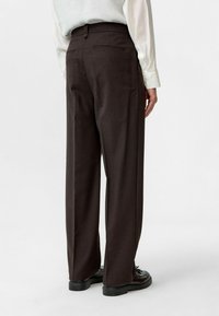 Donkerbruin op maat gemaakte broek met een rechte fit, voorzien van een knoopsluiting en twee achterzakken. De stof heeft een gladde textuur.