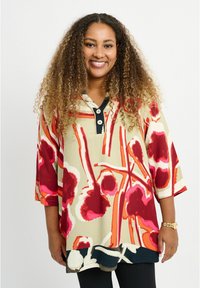 Tunic a motivi crema e rossi con maniche larghe, caratterizzata da un colletto nero e bottoni, con orlo arrotondato e audace design floreale astratto.
