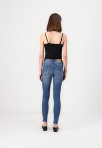 Černý top na tenké ramínka s tmavě modrými skinny jeans, které mají texturovaný povrch a světle hnědou koženou nášivku na zadním pásu.