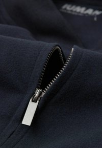 Marineblauwe gezipperde jas met een gladde textuur en een metalen rits. De kraag heeft een subtiele vouw, die het ritsdetail benadrukt.