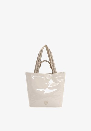 Sac fourre-tout beige brillant avec deux poignées en tissu imprimées d’un texte répétitif, et un petit logo métallique circulaire en bas au centre à l’avant.