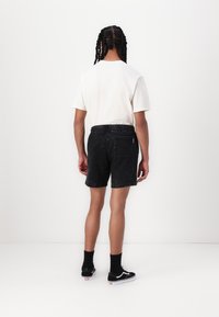 Shorts en denim noir à coupe décontractée, avec une taille élastique et une poche au dos. Associés à un T-shirt blanc et des baskets noires.