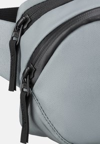 Hellgraue Stofftasche mit zwei schwarzen Reißverschlüssen und Zippern, Nahaufnahme zeigt Textur und Nahtdetails.