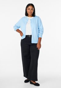 Svijetloplavi kardigan s dugmadima i rebrastim manšetama, uparen s bijelom majicom i crnim hlačama širokih nogavica, nošen s crnim ravnim cipelama.