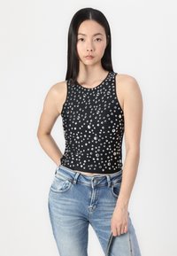 Top sans manches noir avec un motif de clous ronds transparents, associé à un jean en denim bleu clair. Texture lisse et design ajusté.