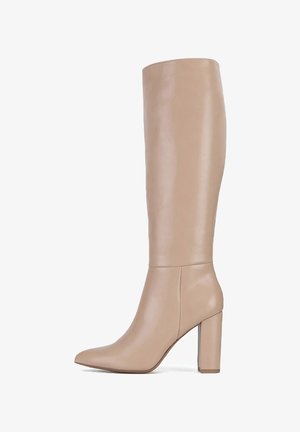 Bota alta de cuero beige con tacón alto y puntera puntiaguda, diseño elegante que llega justo por debajo de la rodilla.