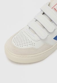 Valge nahast toss halli seemisnahast detailide, võrgustavad perforatsioonide, kolme takjakinnitusega ja tekstuurse kummist tallaga. Omab sinist logodetaili.