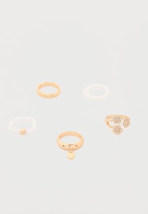 Fem ringer på hvit bakgrunn: to gullringer med hjerteanheng, en gullring med blomster, og to hvite perleringer.