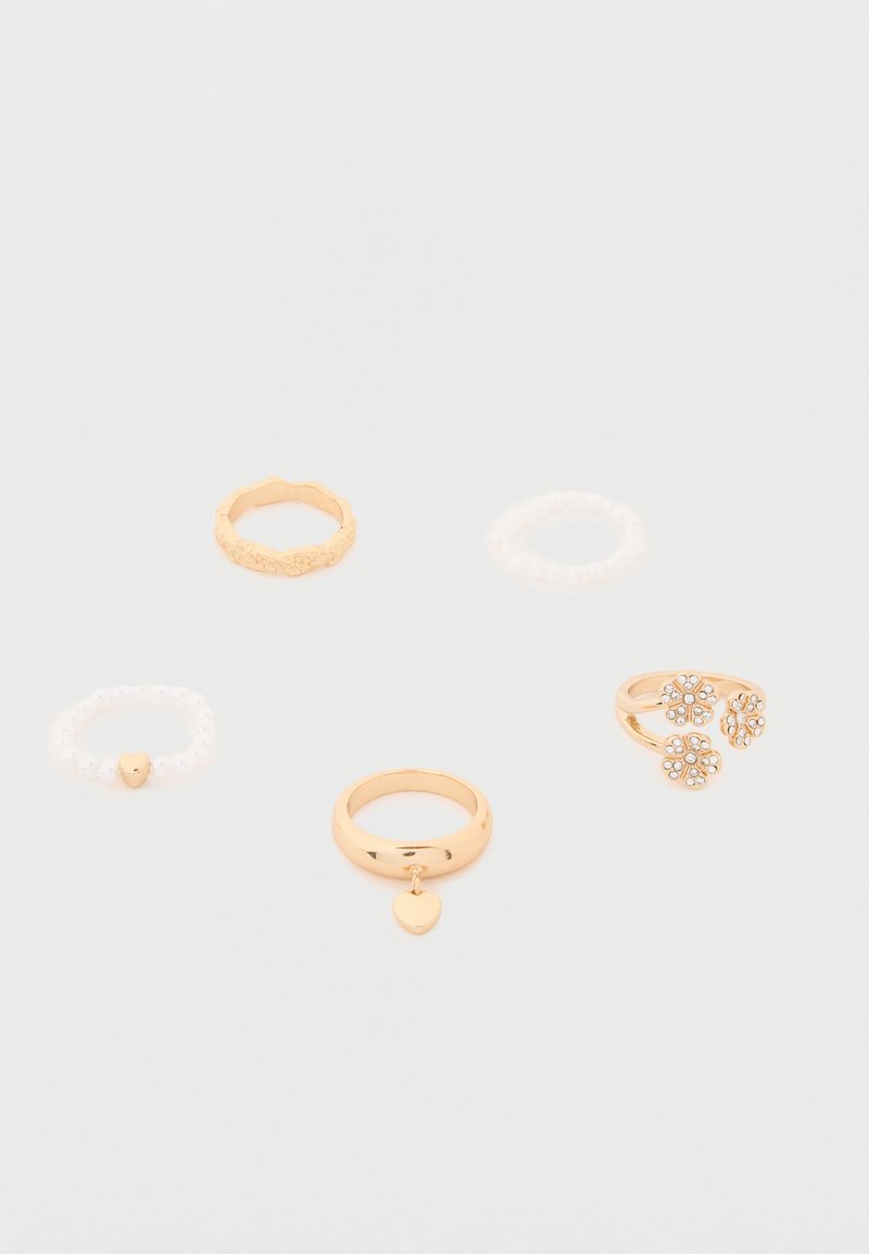 Πέντε δαχτυλίδια σε λευκό φόντο: δύο χρυσά με καρδιές, ένα χρυσό με λουλούδια και δύο λευκά με χάντρες.