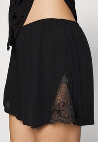 Schwarze Shorts aus weichem Stoff, mit seitlicher Spitzenborte am Saum und einem elastischen Bund für eine bequeme Passform.