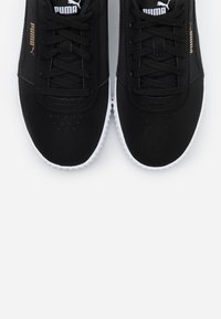 Mustat nauhalla kiinnitettävät sneakerit, joissa on synteettinen päällinen, kullanvärinen PUMA-logo ja valkoinen kumipohja. Liukas pinta ja pyöreä varvastyyny.