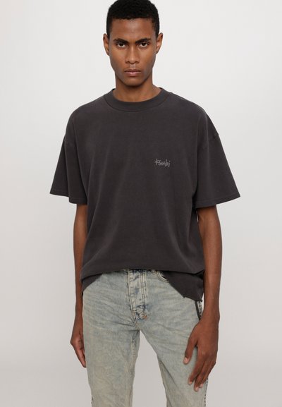 Czarna szara, duża koszulka z bawełny, z okrągłym dekoltem i krótkimi rękawami. Subtelne logo "ksubi" na piersi. Jasnoniebieskie dżinsy.