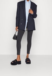 Blazer negro de doble botonadura sobre una camisa azul claro, combinado con jeans ajustados oscuros y sandalias negras de plataforma con detalles recortados y peluche.