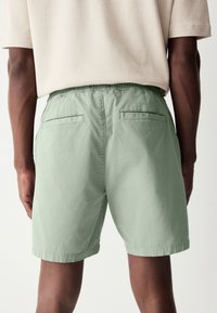 Shorts vert clair en tissu texturé avec une taille élastique, dotés de deux poches arrière et d'une coupe droite.
