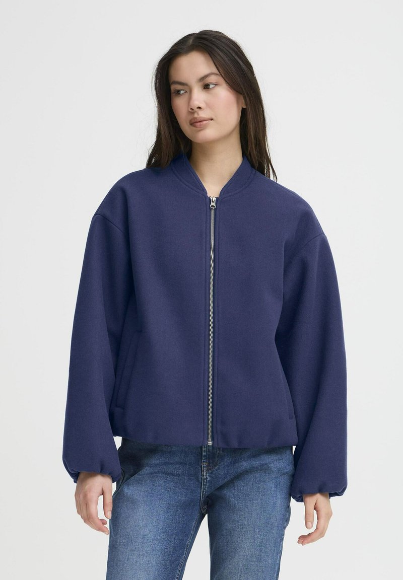 Jūras spēku bumbvedēja jaka ar priekšējo rāvējslēdzēju, apaļu kakla izgriezumu un oversize piedurknēm. Iegūta no mīksta auduma, ar vaļīgu piegriezumu un sānu kabatām.