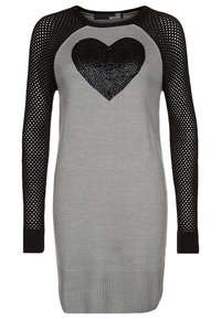 Robe en tricot grise avec des manches en résille noires, présentant un grand motif de cœur en sequins noirs sur le devant. Ourlet côtelé en bas.