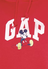 Sudadera roja con capucha que presenta un logo blanco de "GAP" y un gráfico de dibujos animados de Mickey Mouse. El material es suave con una textura lisa y capucha con cordón ajustable.