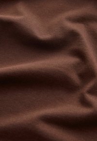 Material maro cu falduri moi și textură fină de tricot vizibilă, prezentând variații de lumină naturală și umbră pe suprafață.