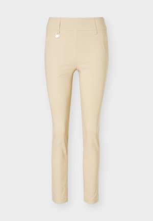 Beige slim-fit ankle-length pants with a mid-rise waist and a small metal decorative element near the waistband.