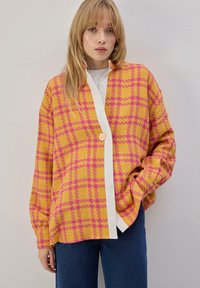 Veste oversize à carreaux jaune et rose avec garniture blanche contrastante et fermeture par boutons. Texture douce et manches larges, assortie à un jean.