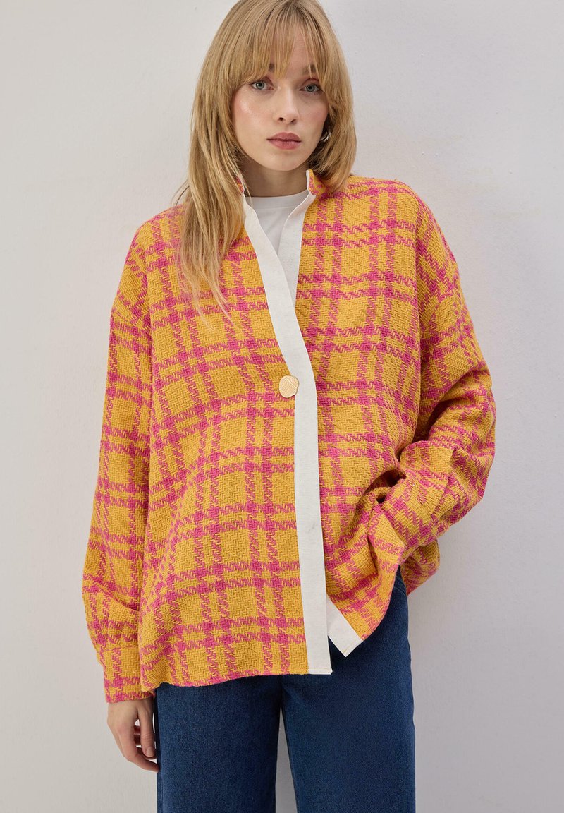 Veste oversize à carreaux jaune et rose avec garniture blanche contrastante et fermeture par boutons. Texture douce et manches larges, assortie à un jean.