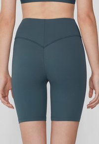 Shorts de vélo taille haute, en teal foncé, fabriqués dans un tissu extensible. Présentent un design ajusté, une finition sans couture et une texture lisse.