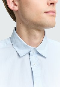 Lichtblauw gestreept shirt met een klassieke kraag, knoopsluiting en zachte stoftextuur, die subtiele verticale lijnen benadrukt.