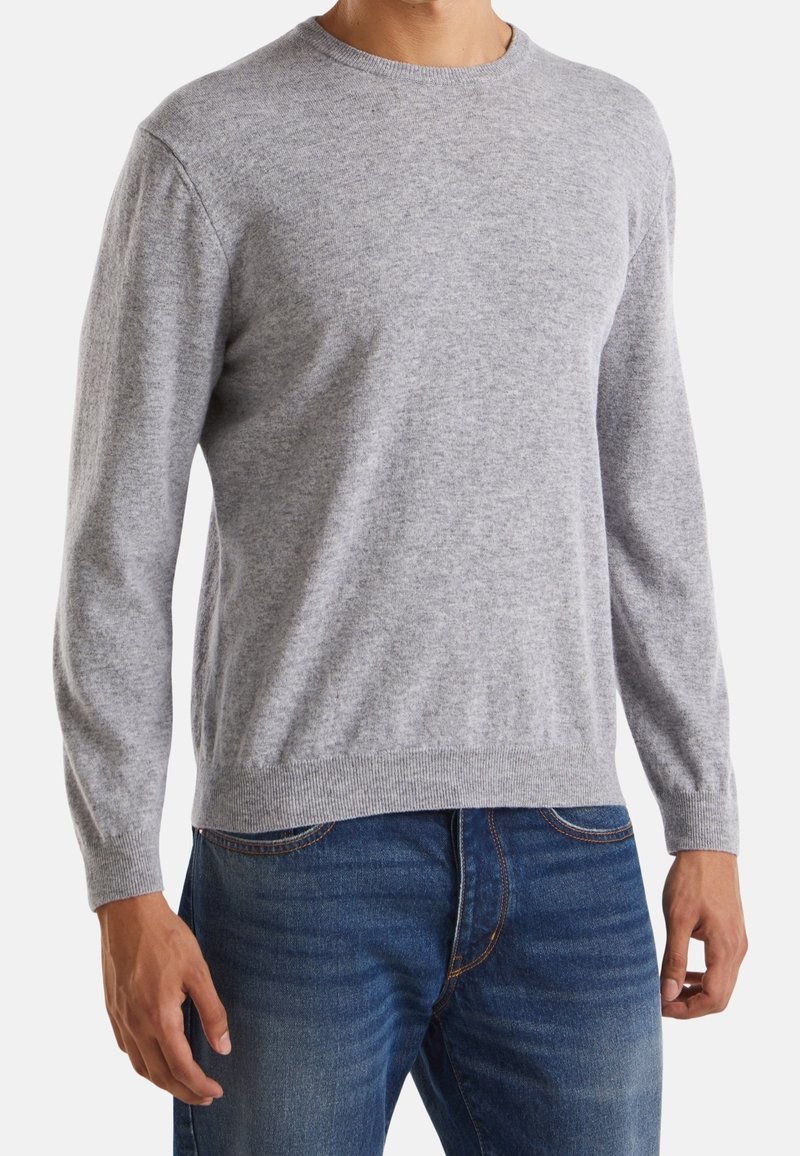 Ljusgrå tröja av mjukt material med rund halsringning och långa ärmar, tillsammans med blå denimjeans.