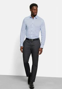 Hellblau gemustertes Hemd mit langen Ärmeln und Knöpfen, kombiniert mit dunkelgrauen Hosen und schwarzen Schuhen, dazu ein schwarzer Gürtel.