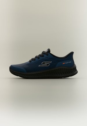 Une basket de sport bleu marine et noire avec des lacets noirs et une semelle amortissante, marquée avec les textes "S" et "Slip-Ins" sur le côté.